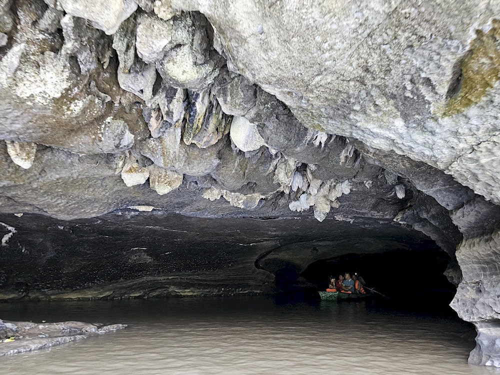 The cave’s mouth is low, dark, and narrow, evoking a sense of mystery as if entering another hidden world